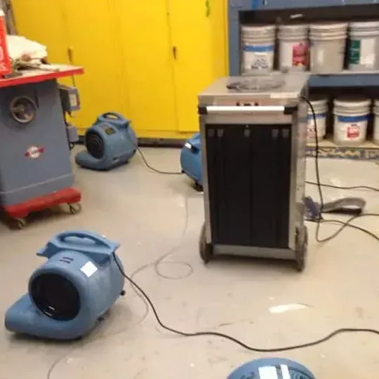 A dehumidifier and air movers drying a workshop floor